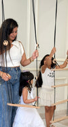 Woman and two young girls playing with a wooden swing and climbing toy indoors.
