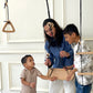 Woman and two children interacting with wooden toys in a room with white walls and framed pictures.