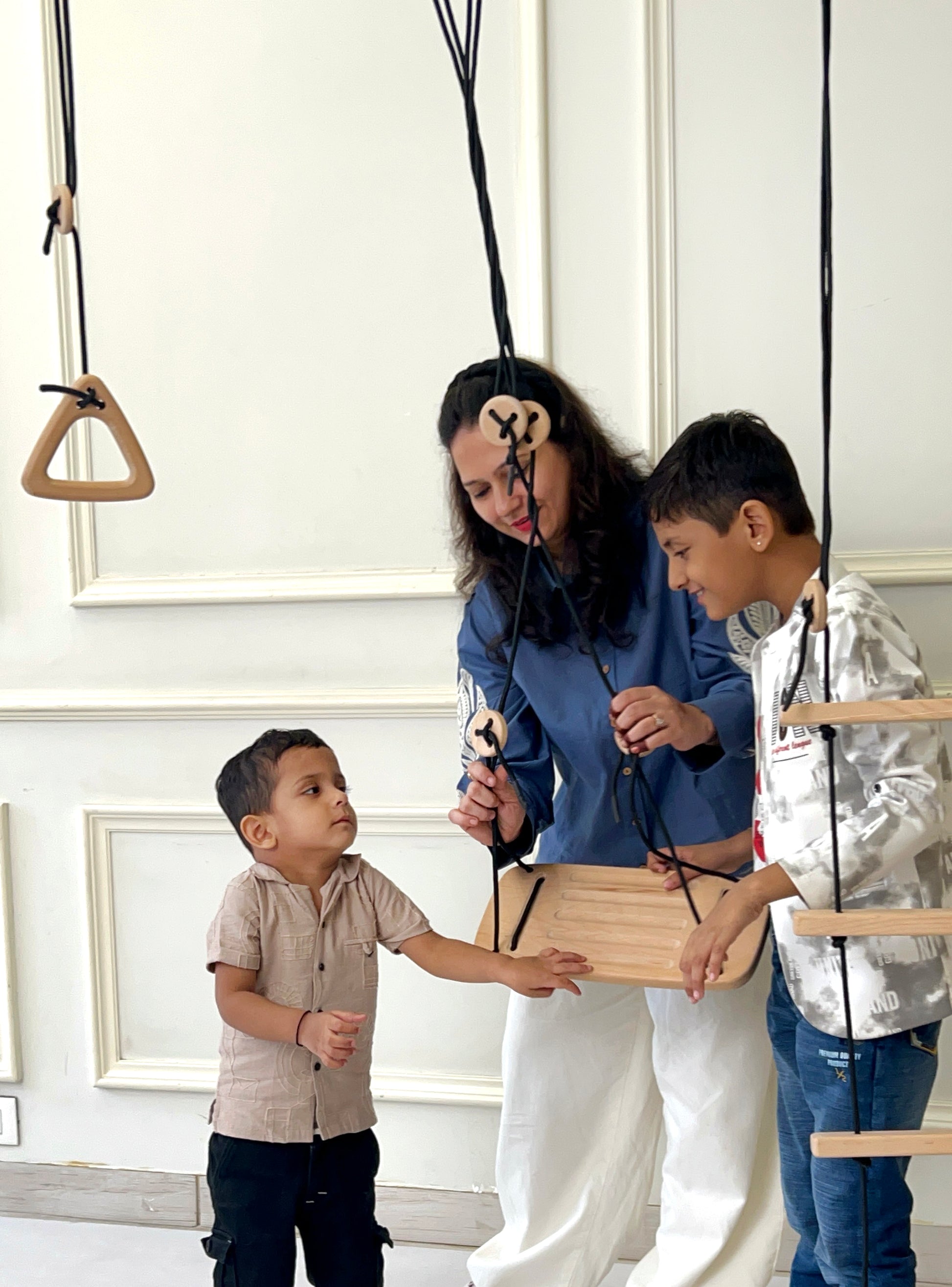 Woman and two children interacting with wooden toys in a room with white walls and framed pictures.